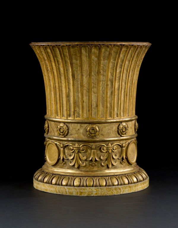 The upper rim carved with egg-and-tongue motif.  The main body fluted with gilded highlights.  The lower section set with giltwood roundels and anthemions on a marbleized ground.  The whole raised on a carved and molded plinth base.