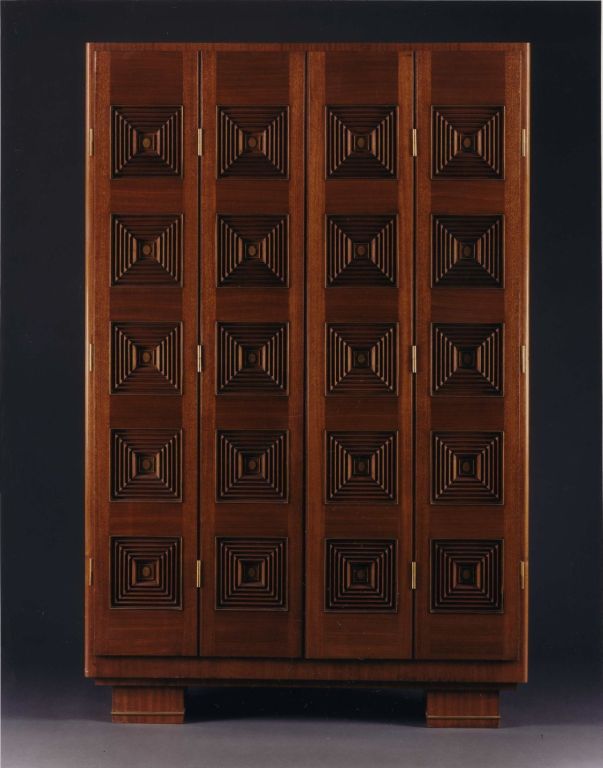 The articulated doors with stepped edges with concentric square mouldings, each with brass ovals at the center, of which the two central ovals are monogrammed with that on the right side moving to reveal a keyhole. The doors opening to reveal a