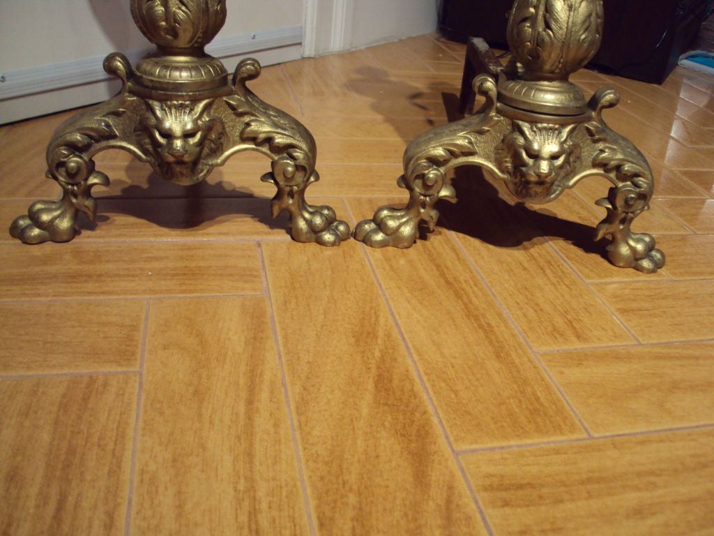 ANTIQUE PAIR OF BRONZE BRASS ANDIRONS WITH LION HEAD, CLAW FEET AND ROCOCO STYLE LEAVES AND DECORATIONS.