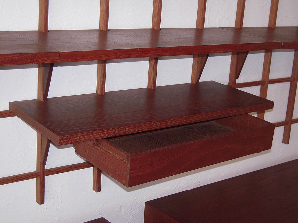Modern and minimalist design of this display unit or bookshelf features a double grid support system made of teak, joined together and attached directly to the wall where various size platforms cantilever. One center drawer with attached shelf.