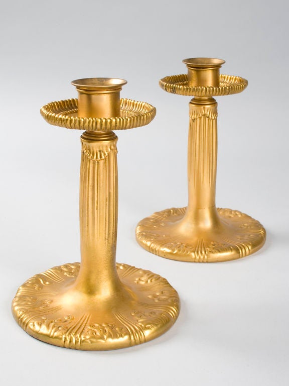 A pair of Tiffany Studios New York gilt bronze candlesticks, featuring an embossed decoration of flames around the base. Signed, “Tiffany Studios New York.”