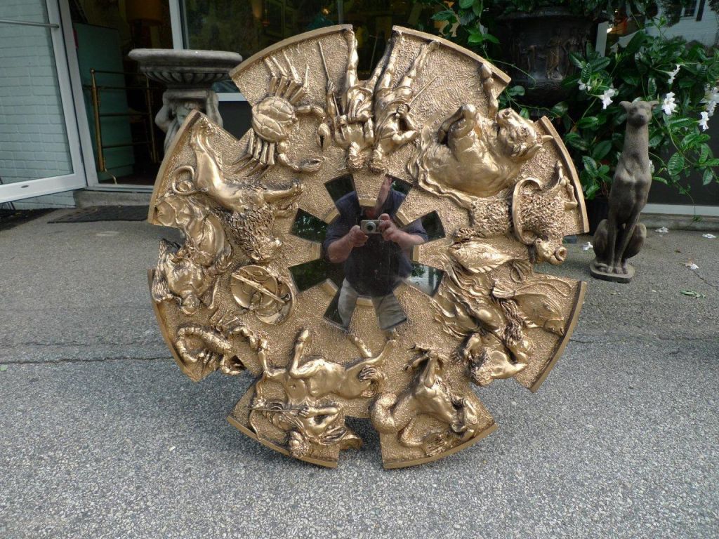 Gold finished hand poured cast resin and fiberglass 3D Brutalist style framed round wall mirror with relief figures from the Zodiac.  36 inches diameter.

Crenelated design reminiscent of mirror from famous renaissance painting Arnolfini