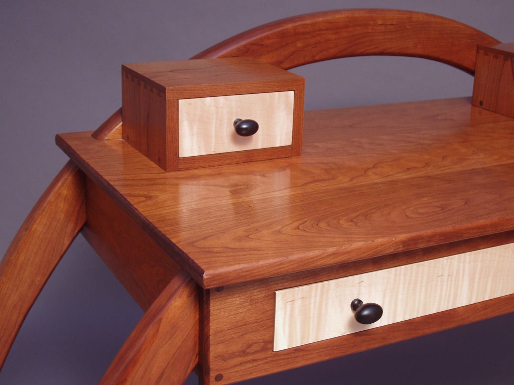 Solid black cherry writing desk with curly maple drawer fronts. The rear legs give the appearance of a continuous arch that pierces one side, continues on top and returns to the floor on the opposite side. All legs are removable for transport and