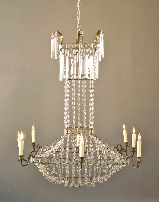 A very rare and unusual French chandelier with eight bronze arms and crystal beading.  The top is decorated with tole acanthus leaves holding flat spear prisms with matching prisms on the top section below.  Originally candle.