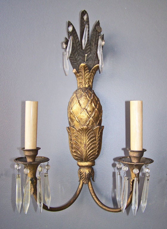 A decorative set of four carved gilt wood two arm sconces with tole leaves and prisms.