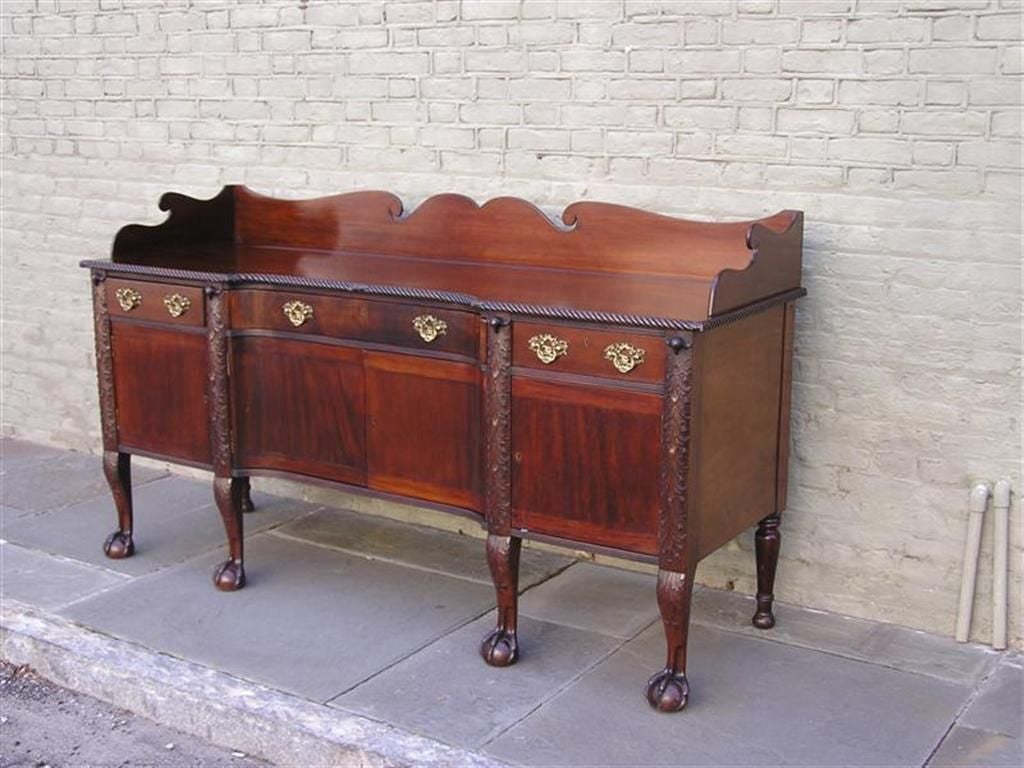 Irish Cuban mahogany three drawer sideboard with carved scrolled gallery, gadrooned molded edge, carved eagle heads, flanking lower cabinets, original brasses, and terminating on acanthus carved legs on claw & ball feet.  Mid 19th Century.   

