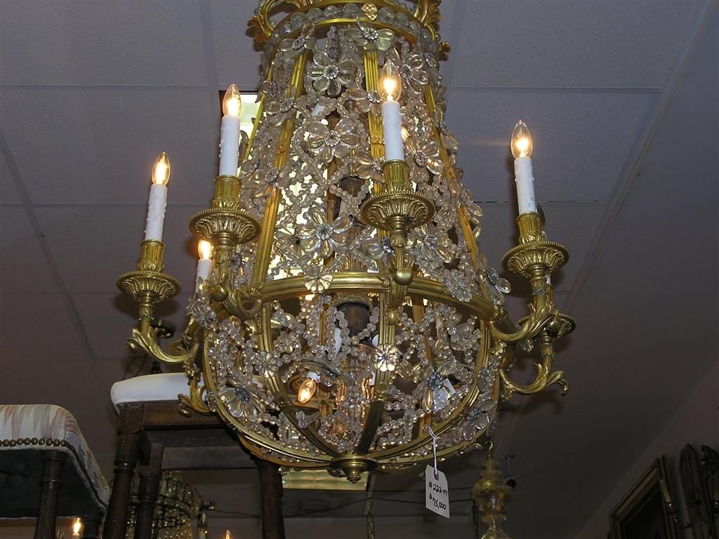 French Baccarat gilt bronze and crystal sixteen light chandelier with a scrolled foliage canopy, exterior intertwined crystal floral beading, original scrolled floral candle bobeches, interior electrified crystal faceted column, and resting on a