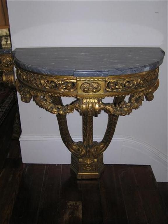 Pair of French demi-lune gilt carved wood consoles with floral swags, acanthus carvings, and grayish white vane marble tops . Consoles can mount to wall for support . Late 18th Century.