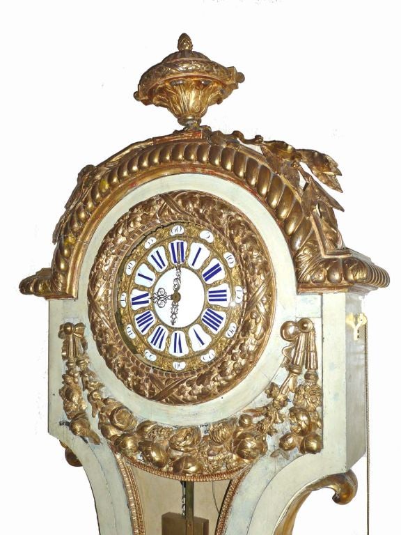 Important Louis XV Giltwood and Polychromed Wall Clock, Circa 1760; the lyre shaped case with an arched top and urn shaped finial over branches of leaves; the single door features a garland of leaves surrounding the clock face; the sides with four