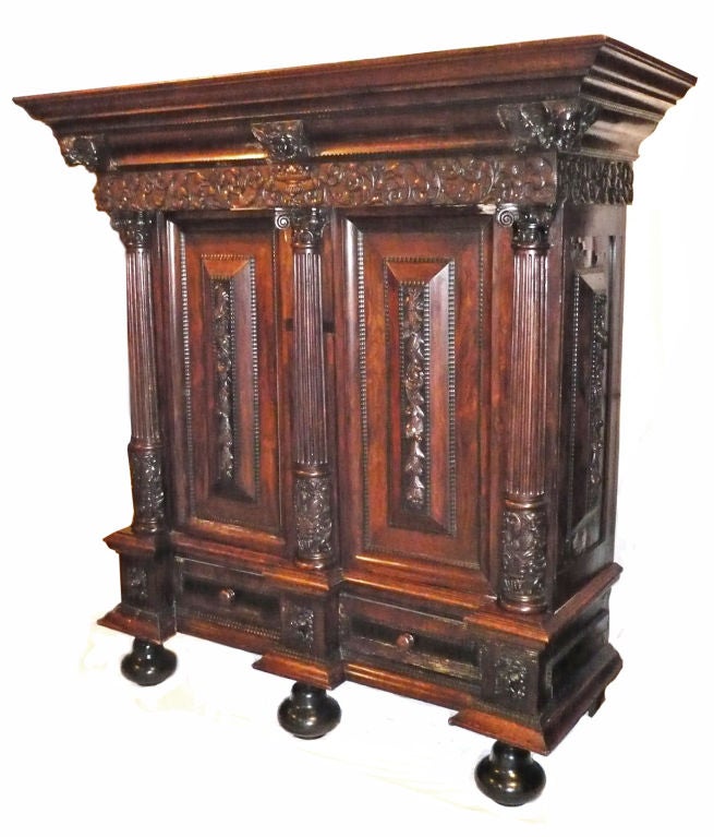 in the high baroque manner featuring a molded cornice with applied carved cherubs; above a foliate carved freize and paneled doors separated with columns and similarly embellished with flora; over two drawers and raised on ebonized bun feet. <br />
