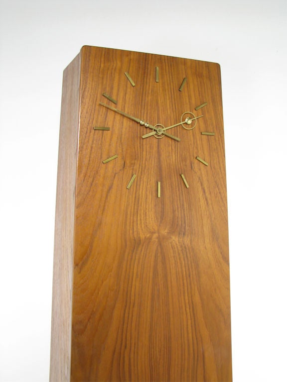 Rare Danish teak case clock ca. late 1950s – early 1960s.   Highly figured bookmatched teak grain.  Delicate carved platform with brass beaded spacers lends cabinet appearance of floating.  Door opens to reveal shelved storage.