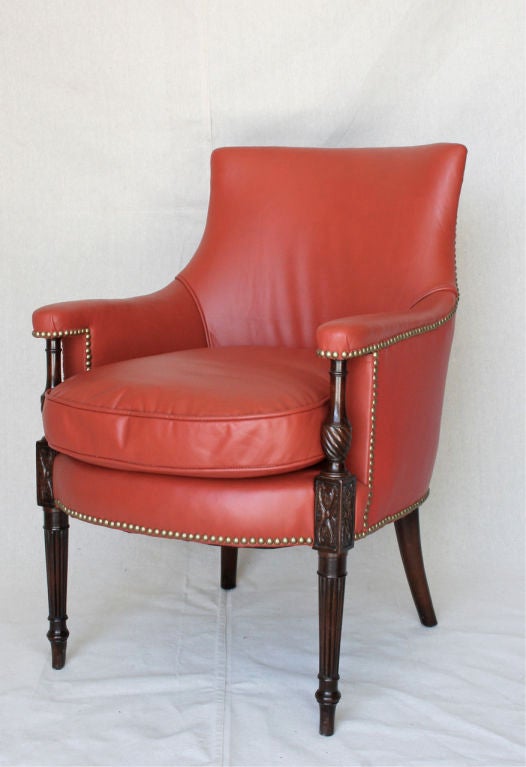 A newly upholstered bergere with finely turned and carved mahogany legs upholstered in a soft tomato red leather and accented with brass tacks.