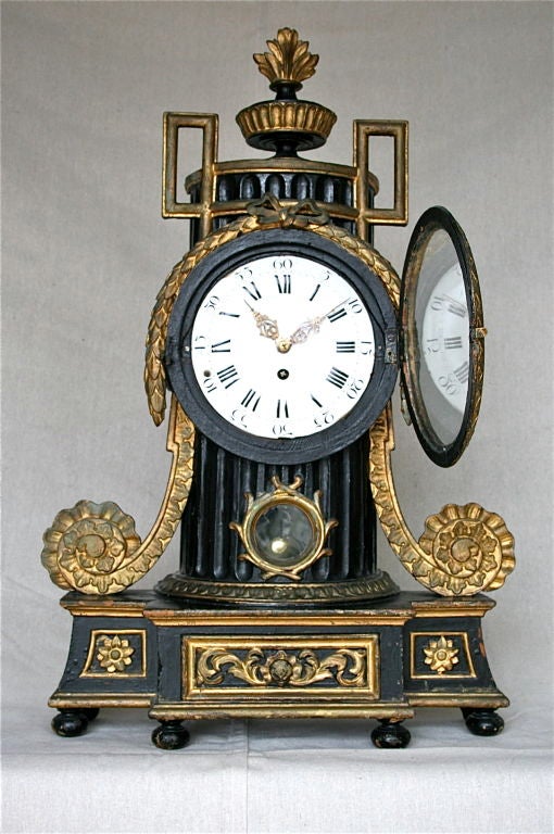 Large scale German Baroque black lacquered and gilt decorated clock with glazed circular enamel dial having both Roman and Arabic numbers accented with carved foliate scrolls. Sitting on a flared rectangular plinth base.