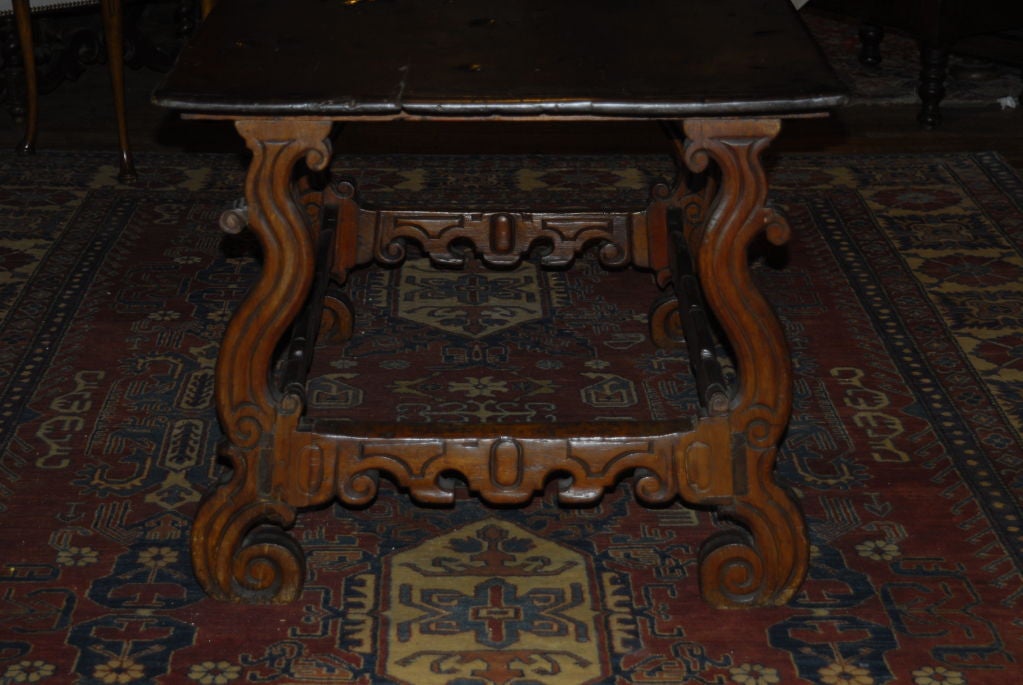 A robustly carved Spanish/Portugese Colonial Baroque stretcher table with a wide one board top. This mahogany or padouk table has a deep rich color and great deeply carved scrolls.  Originally purchased in Brazil