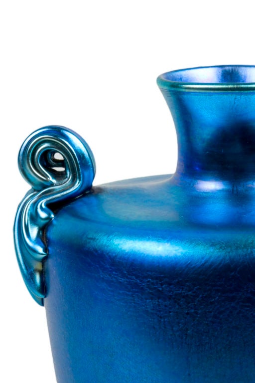 A Tiffany Favrile Iridized Blue vase decorated with two applied scroll handles and heavily iridized blue body. The vase is signed, 