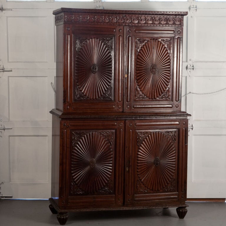 Indo-Portuguese cabinet in solid rosewood with typical sunburst patterned carved doors and other carved details. Interior has single shelf on top and two shelves in bottom cabinet.