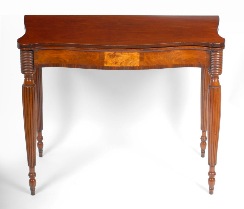 This attractive table has a serpentine shaped and figured mahogany top with outset corners.  The flip over top is supported by a rear swing leg and opens to form a playing surface.  The top rests above a shaped apron veneered with richly grained