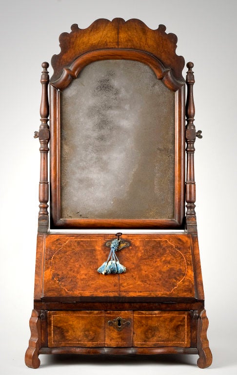 This wonderful dressing mirror has a wonderful molded Rococo form and a mellow historic surface.  The tombstone-from mirror has a raised burled veneer crest with half round molded frame and original looking glass.  The frame pivots between turned