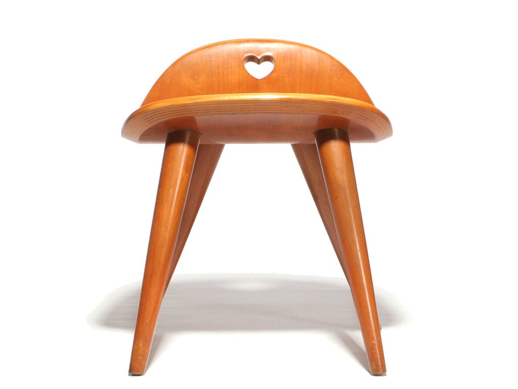 A scoop seat stool with a heart shaped cutout with splayed, tapered dowel legs.
