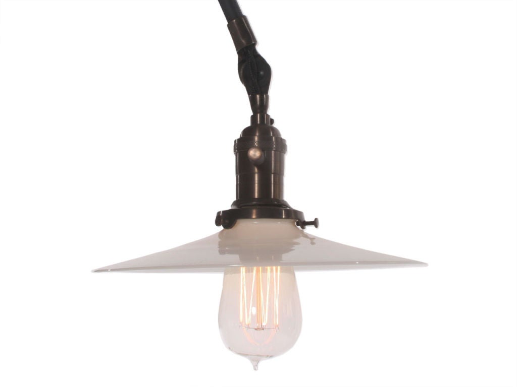 A patinated ceiling fixture with articulated arm and single glass disc shade. 