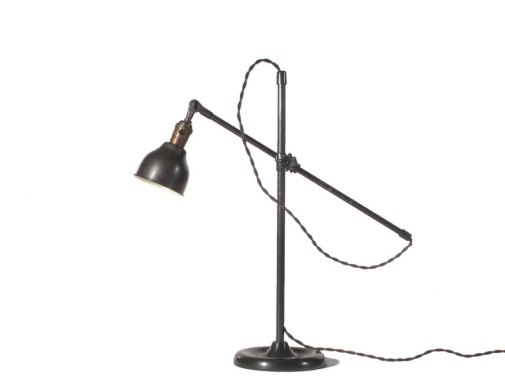 A patinated steel industrial desk lamp with an adjustable arm, a bell form shade and a round moat cast iron base.