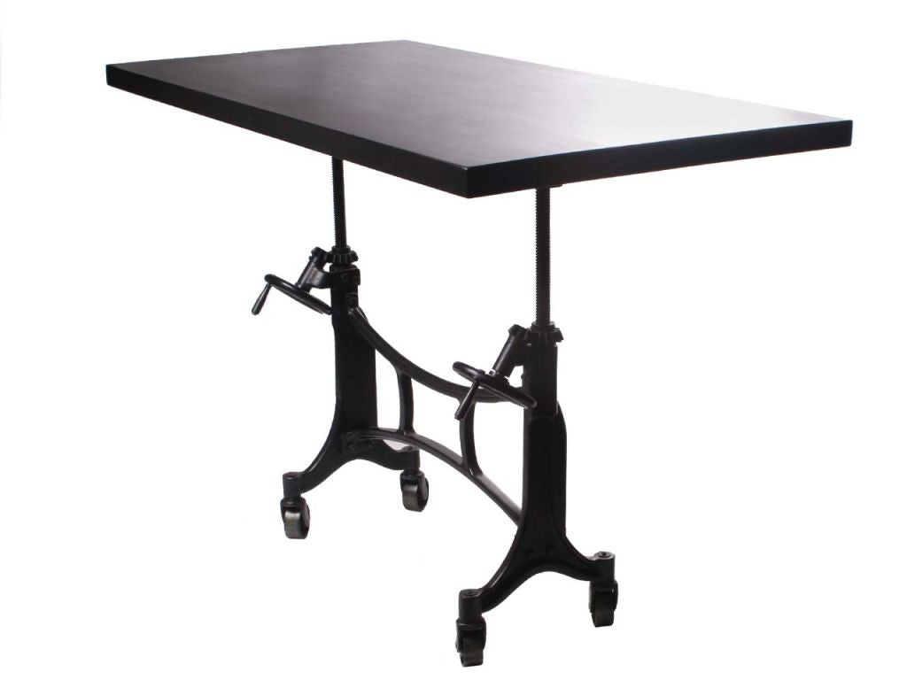 Cette table industrielle sur roulettes est dotée d'un cadre architectural en fonte qui supporte un plateau en acajou huilé, à la fois solide et uni. La hauteur est contrôlée par une paire de manivelles. Utilisée à l'origine comme table d'imprimeur