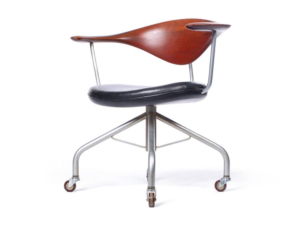 A superb and early 1st generation swivel desk chair having a hand-sculpted floating teak backrest and black leather seat, on a satin chrome base with bakelite casters. A masterpiece of Danish modernism designed by Hans Wegner and crafted by