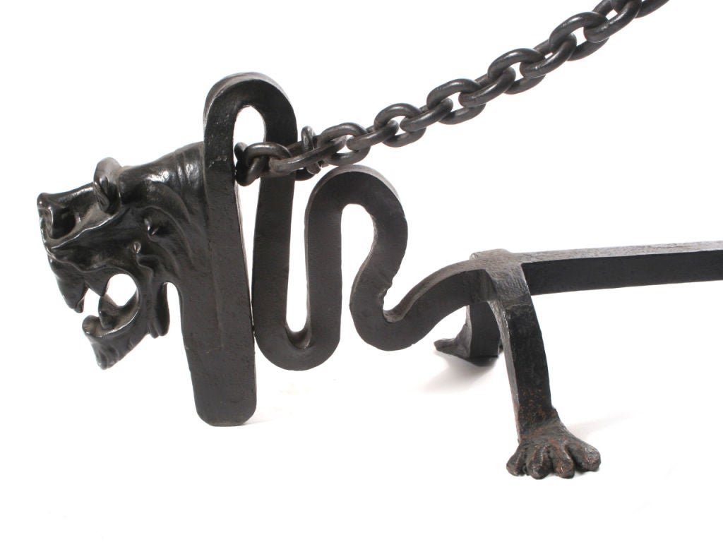 A pair of massive wrought iron andirons with chained dogs on spiked tripod base posts.