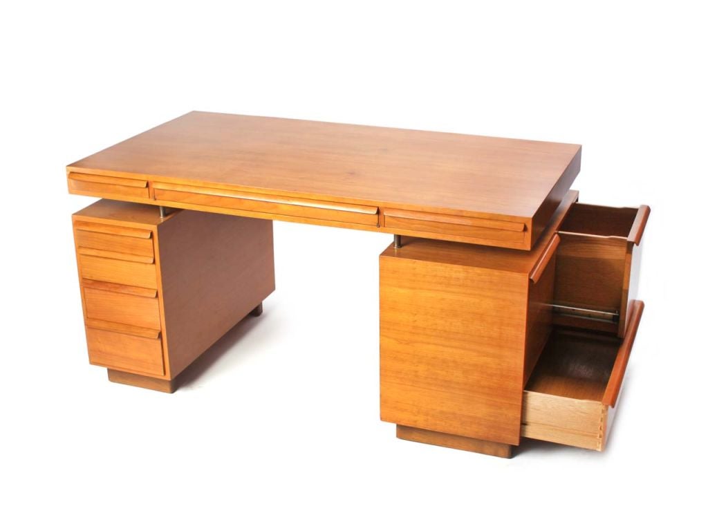 A partners desk in cherry with laminated wood drawer pulls, floating top and a central pass-through flanked by opposing pencil drawers, over a double-sided bank of four drawers and a bank of twin file drawers over one long drawer, on slab feet. <br