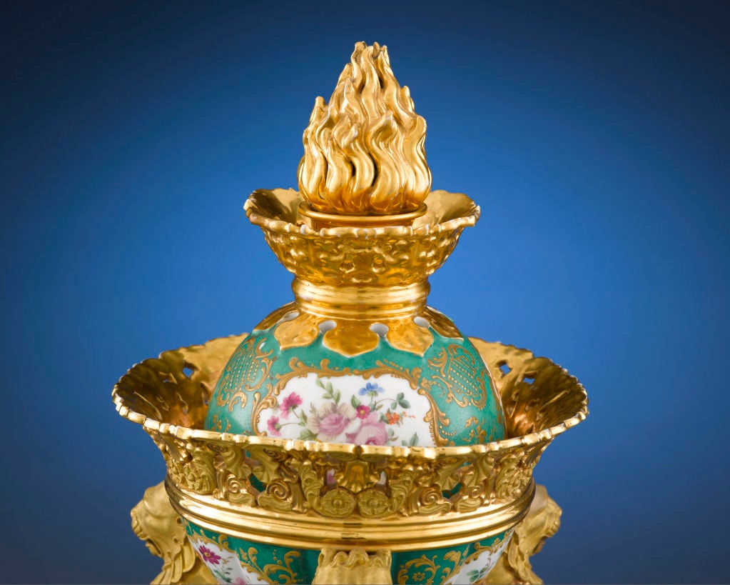 In this stunning porcelain centerpiece by renowned French ceramicist Jacob Petit, a Greco-Roman brazier is re-imagined in dramatic Rococo form. A central container, with floral reserves within gilt scrollwork on a green ground, features a delicate