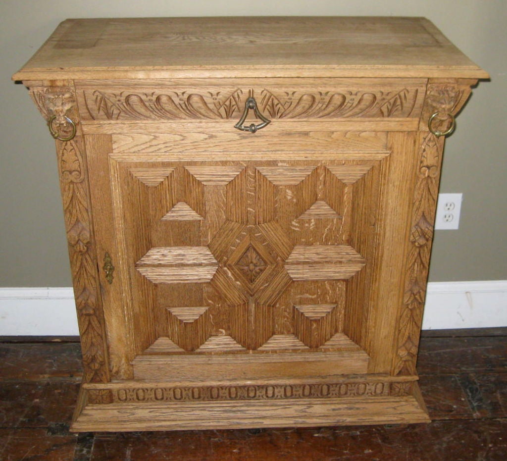 Decorative single door oak storage cabinet bleached to a light patina. Note all the hand carved details throughout and the lion heads on each side of the top drawer. One center shelf below. The cabinet is from the Mechels district of Belgium.