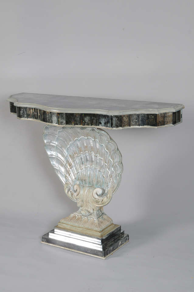 Console, with free-form top of distressed mirror, its conforming apron lined with mirrored tiles, raised on plaster scallop shell in the manner of Grosfeld House, having a distressed painted and parcel silver-gilt finish, graduated plinth base also