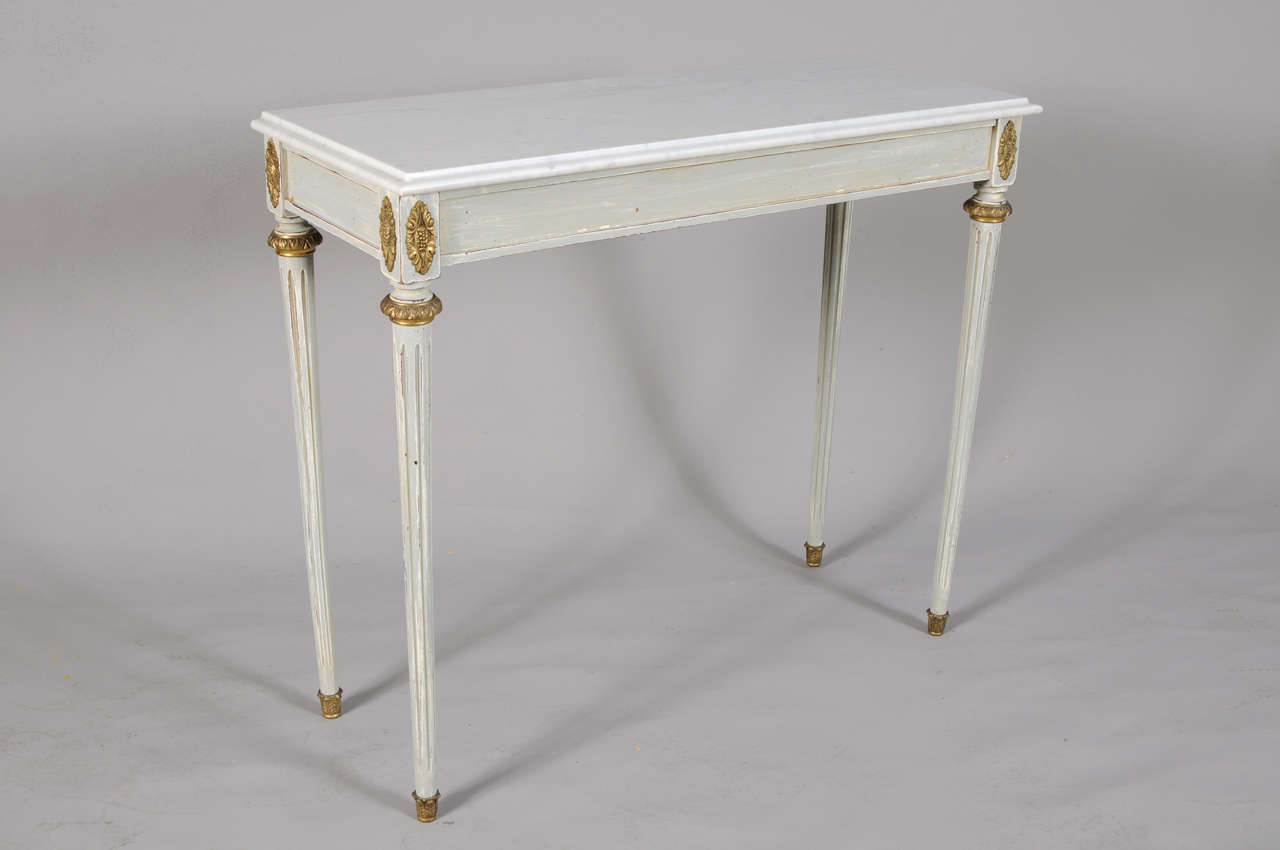 Pair of consoles, in Directoire taste, each having a rectangular top of white marble, on light blue distressed-painted tables base, fielded apron raised on round fluted tapering legs, decorated with bronze rosettes, collars and cups.