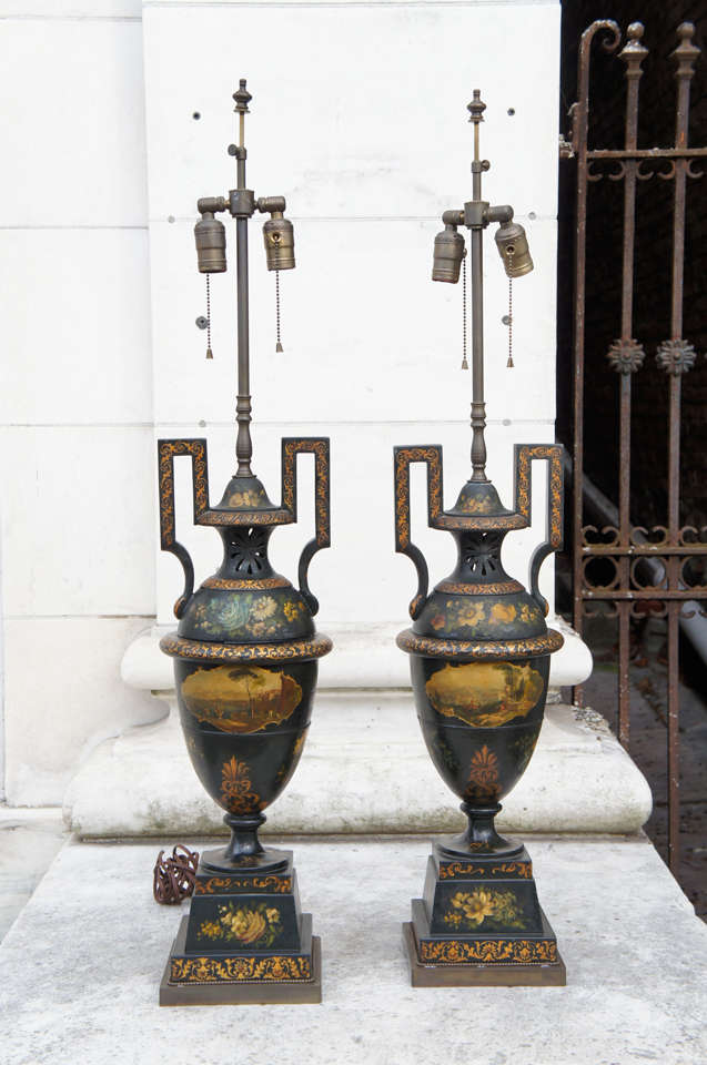 A large and impressive pair of tole urns mounted as lamps. The pieces, originally made as potpourri vases, are very finely painted with detailed and extensive landscapes front and rear. They are further decorated with floral sprays indicating their