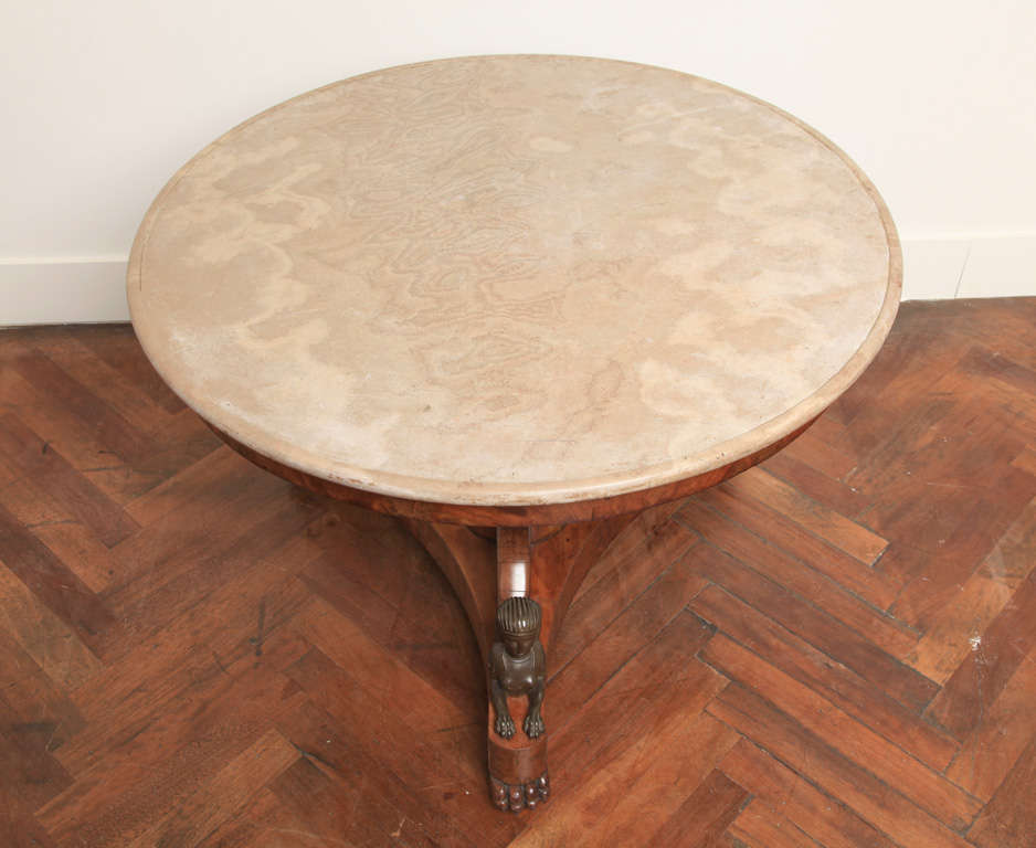 The circular marble top rests on a support raised upon a triangular concave plinth. Each end of the plinth rests on lion's paw feet and castors, and is decorated with a bronze sphinx with 'Nemes' headdress.
