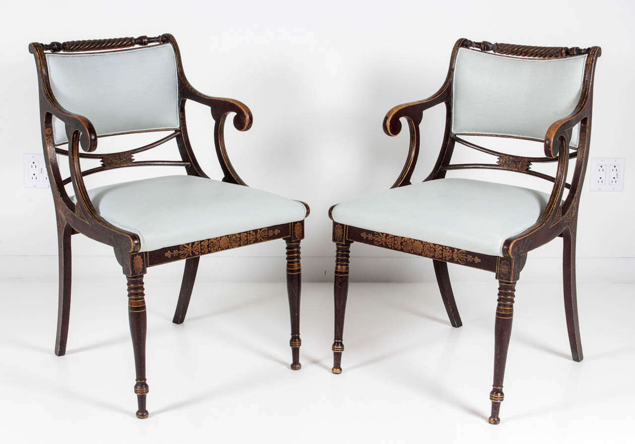 A pair of painted and stenciled Danish Empire open armchairs, Circa 1810-1820, each with a partially upholstered srcolled backrest with a twist turned top rail, straight armrests raised on scrolled supports , drop-in upholstered seats raised on