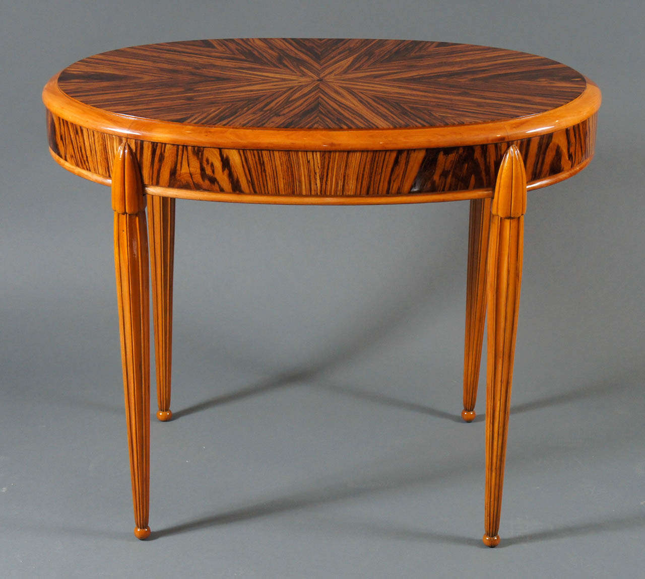 Oval Macassar wood table with striking pattern on top and sides, fluted legs ending in ball feet.