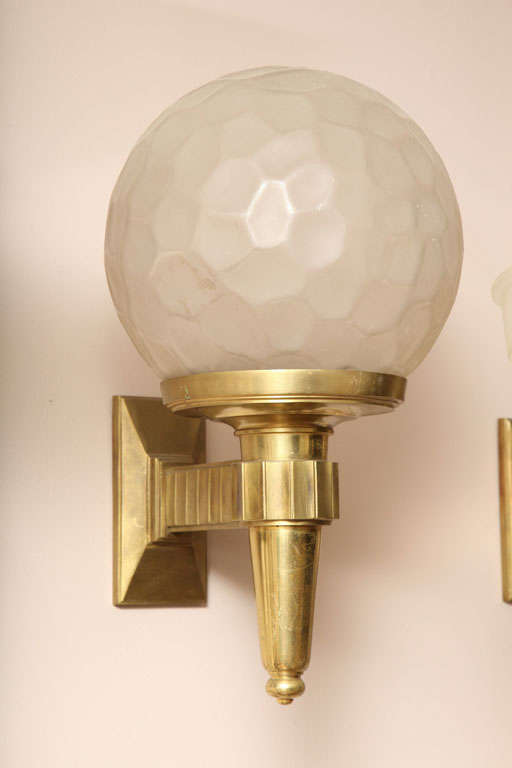 Large pair of one-armed Art Deco wall sconces with bronze bases surmounted by golf-ball shaped frosted glass shades by Genet et Michon, circa 1930.