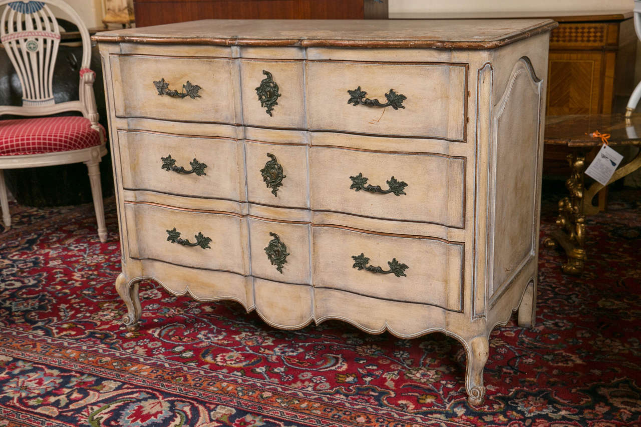 A Swedish paint decorated Louis XV style commode. A finely crafted double serpentine chest commode. This three-drawer commode having bronze mounts and key holes has been meticulously distressed and worn to give the look of an ancient bachelor chest.