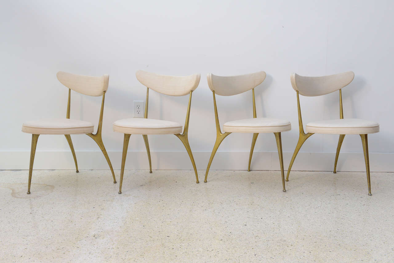 The rounded back of klisoms form, with brass supports over an upholstered seat on three stylized brass legs. These are a very unusual form and quite sculptural in nature. There is a matching table that can be sold together with this set or