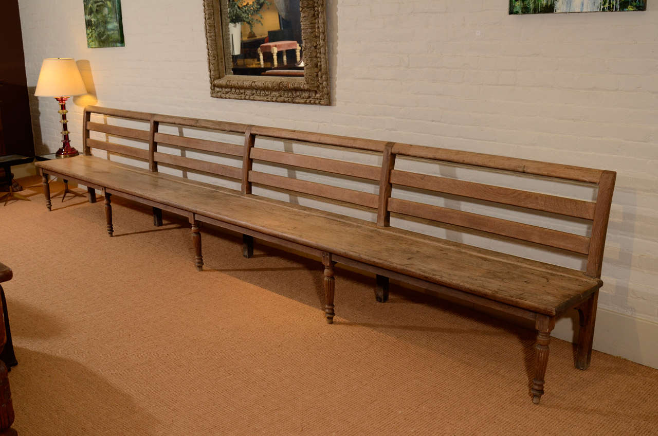 Late 19th Century English carved oak bench. Three-railed back on a wooden seat, supported by five turned and reeded legs. Possibly used as a railroad bench.