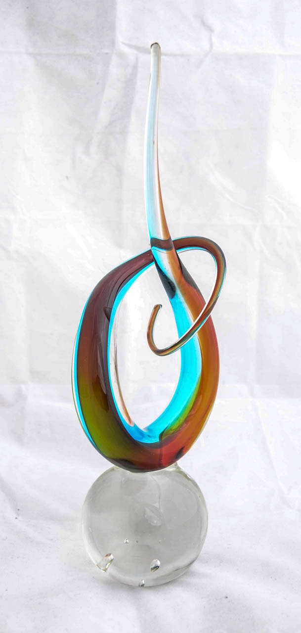 This free-form sculpture is a pulled, tapered knot of multi-coloured strands of glass. set on a solid clear glass spherical base. To the bottom of the base is engraved 