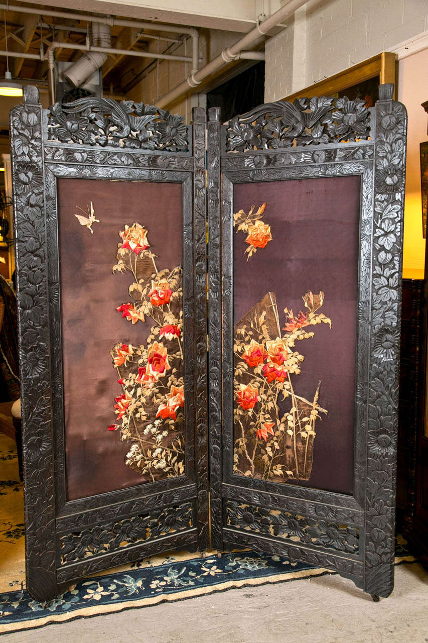 Pair of Chinoiserie style screens, each having an elegantly carved frame decorated with maroon silk and embroidered floral pattern, hinged panels. 

Each Panels Measured: 
30 1/2 inches width by 74 inches height.