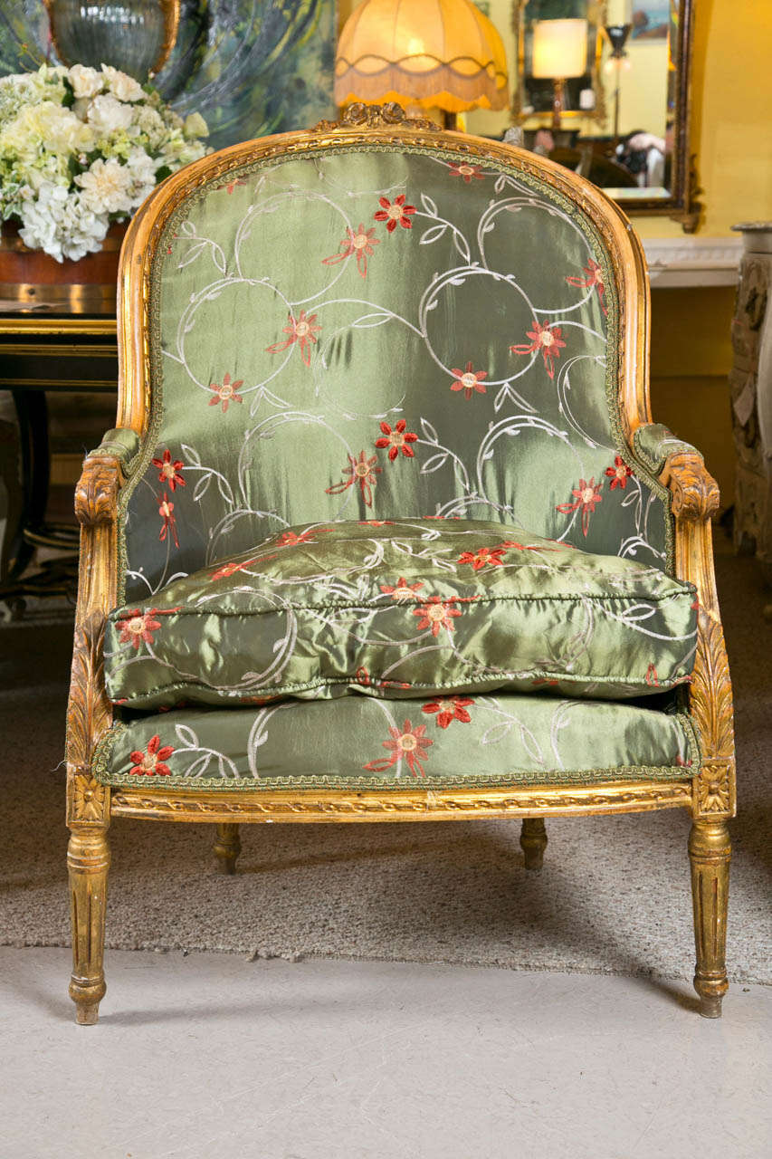 Pair of French Louis XVI style walnut bergere chairs by Jansen, each having a domed back, the frame decorated with annulated and acanthus carvings, cushioned seat and padded arms, raised on short fluted legs.