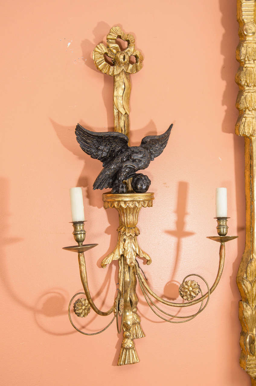 An unusual set of six George III style giltwood and part ebonized eagle motif two-light wall sconces with scrolling candle arms.