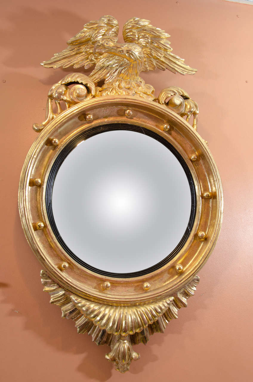 A Regency giltwood convex mirror with eagle and volute crest, folded shell drop, ebonized slip and spherule surround.