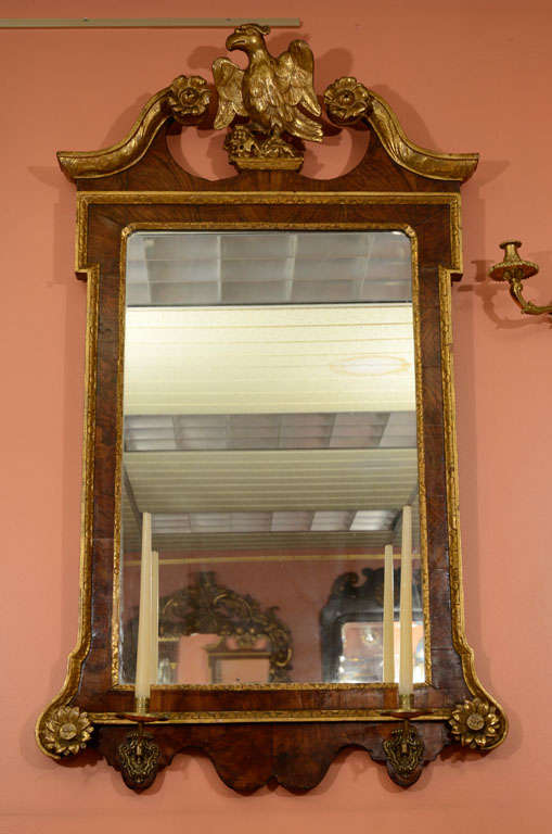 George II walnut and gilt scroll top mirror with carved eagle surmount, carved giltwood rosettes and brass sconce arms.