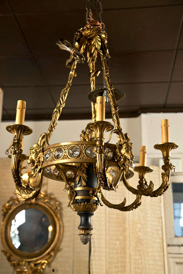 a  6 light polished bronze and patinated chandelier in the Louis xvi style. the  solid arms, carved and chased from the canopy to a ring inset with crystals  and adorned with rams heads, from which emanate  3 sets of double arms of  light. an