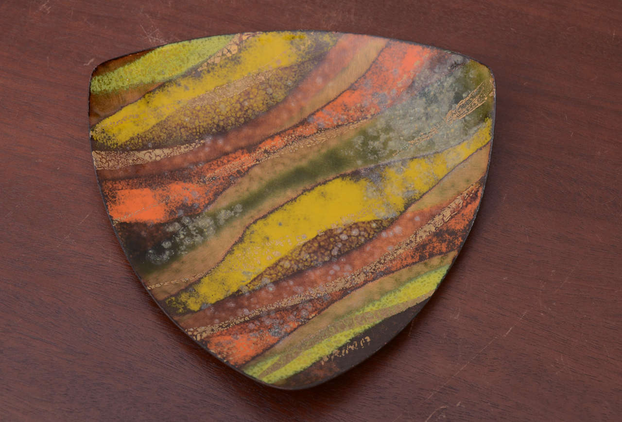 Small enamel dish with green, yellow, orange, bronze and gold design. Corners curve slightly upward. Bottom is black and marked 