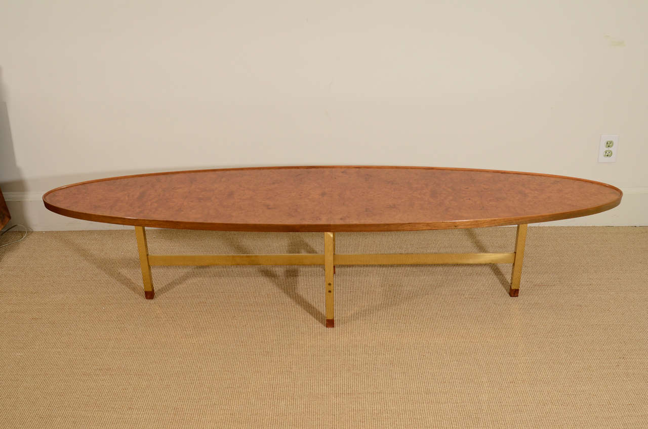 The surfboard shaped table with book matched elm veneers, within an brass band, raised on a brass stretcher.